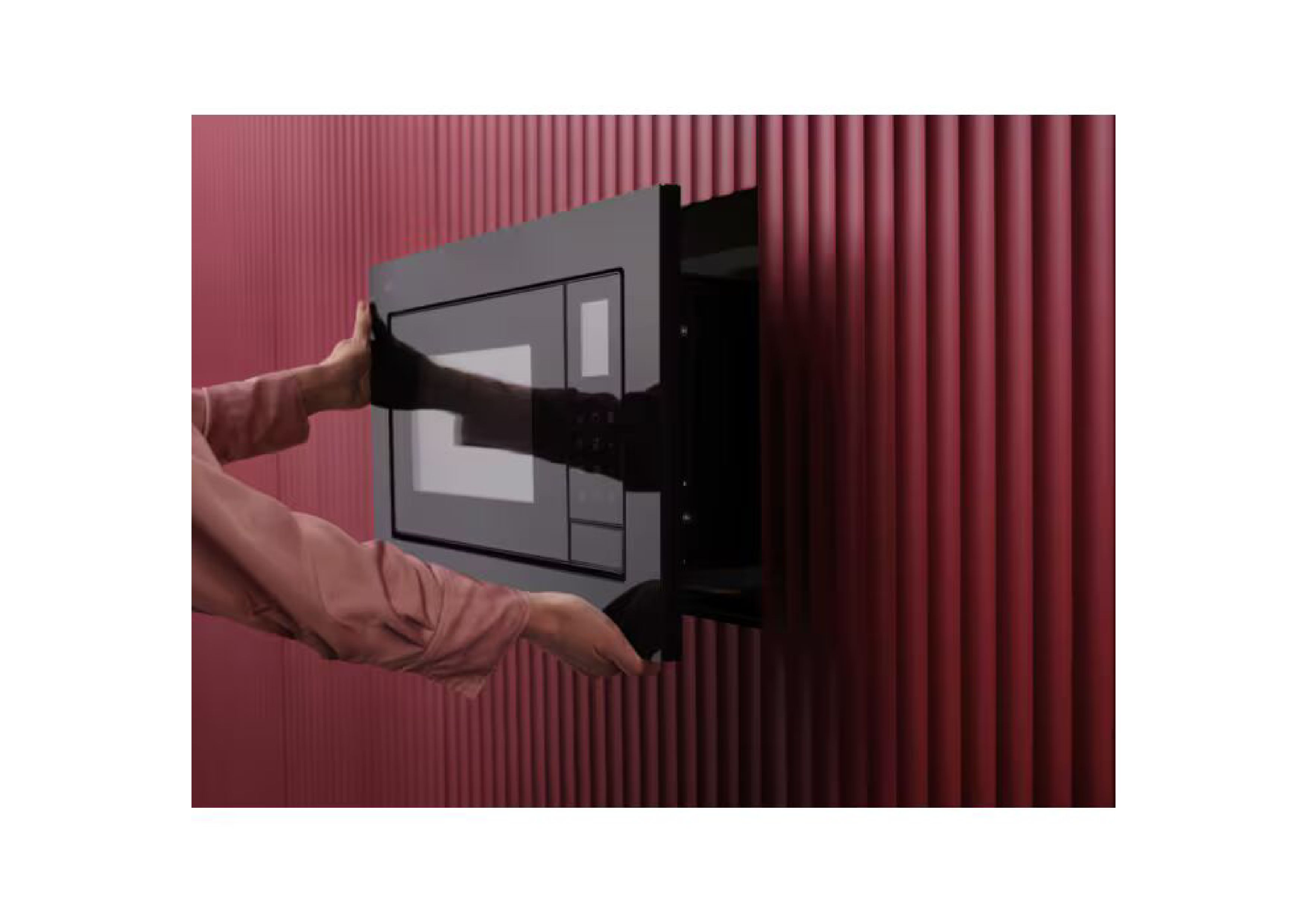Hands installing the black AEG microwave into a red wall niche