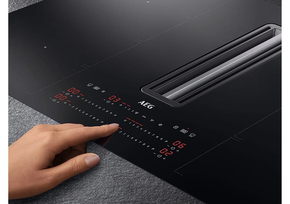 A hand operating the precise slider control on the AEG CCE84779CB induction hob next to the integrated extractor.