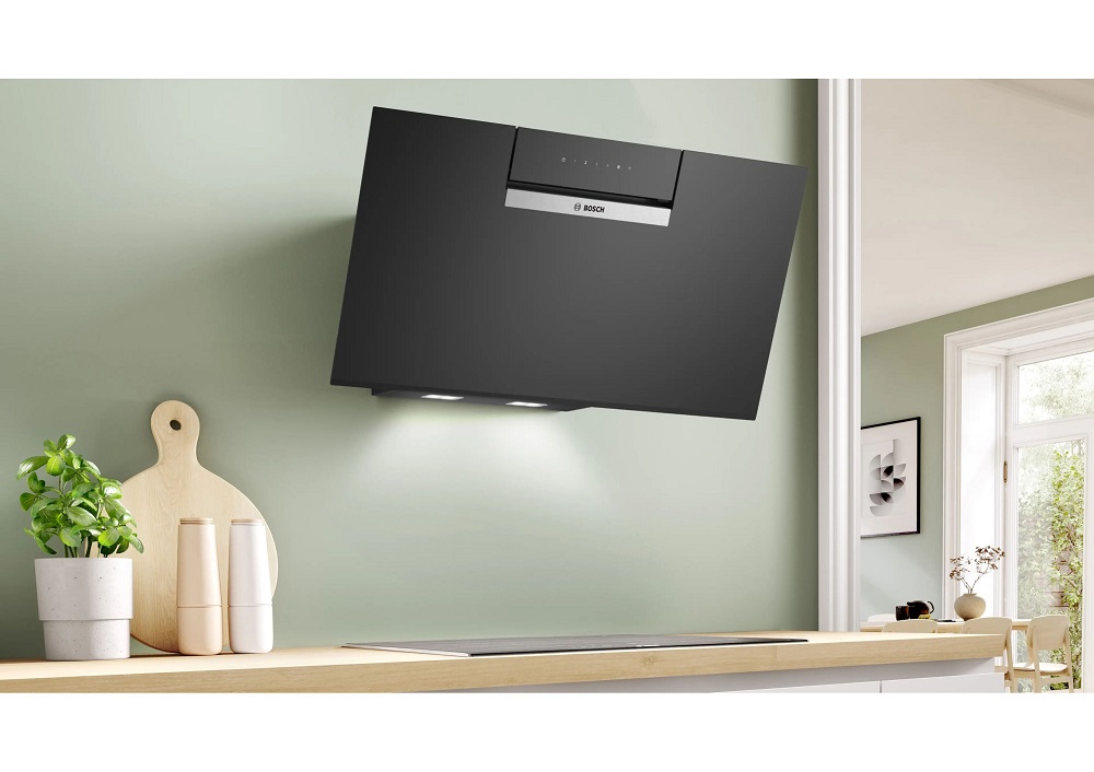 Alternative installation setup of the black Bosch angled hood operating in recirculation mode without a chimney extension, mounted flush against a sage green wall with active LED under-lights.