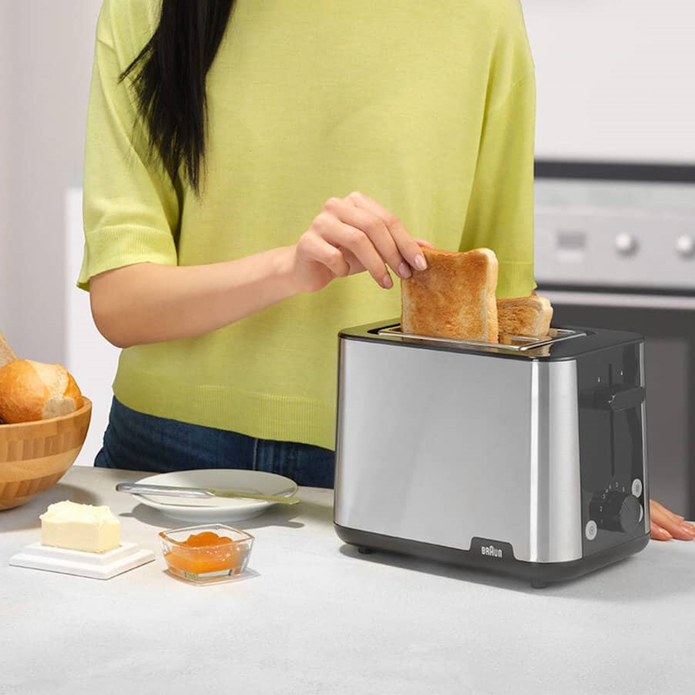 A person removes a golden-brown toasted slice from the Braun toaster; illustration of the high-lift function for safe removal.