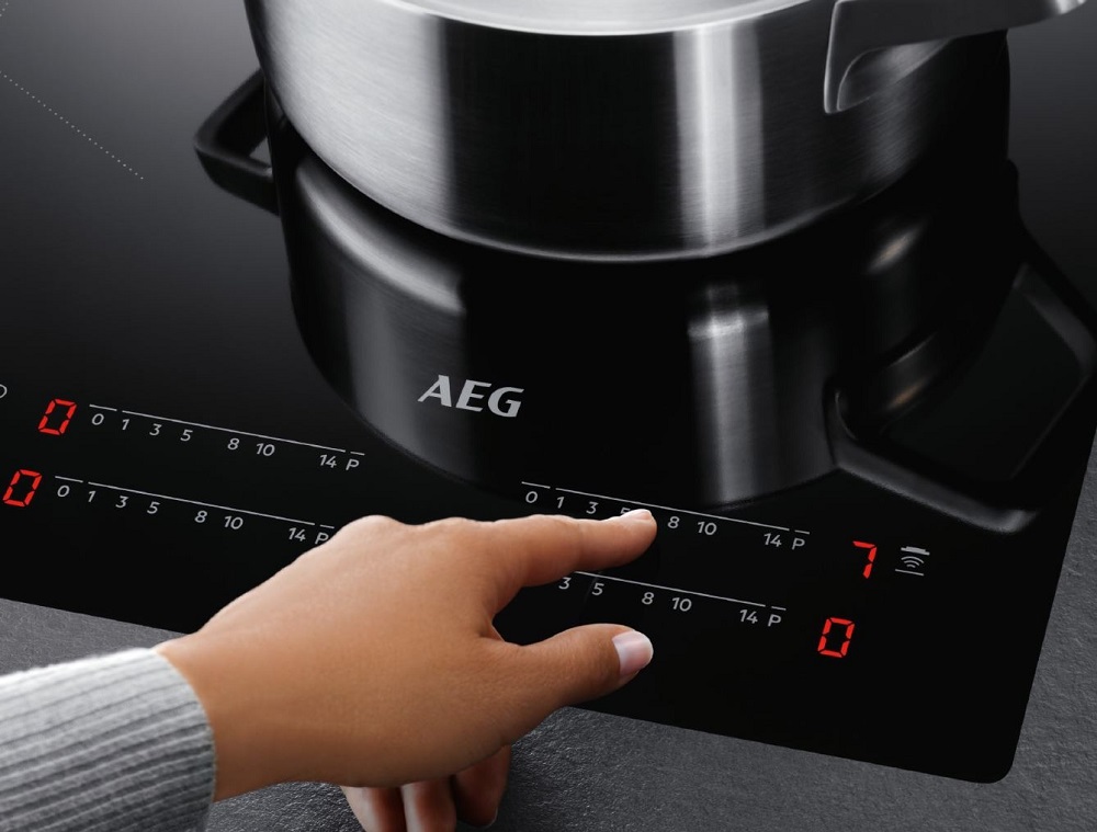 Eine Hand bedient das Touch-Bedienfeld des AEG IKE64441XB Induktionskochfelds, um die Temperatur unter einem Topf einzustellen.
