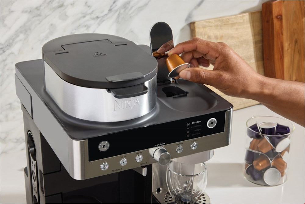 Einlegen einer Kaffeekapsel in das obere Fach der Ninja 2-in-1 Espresso- und Filterkaffeemaschine.
