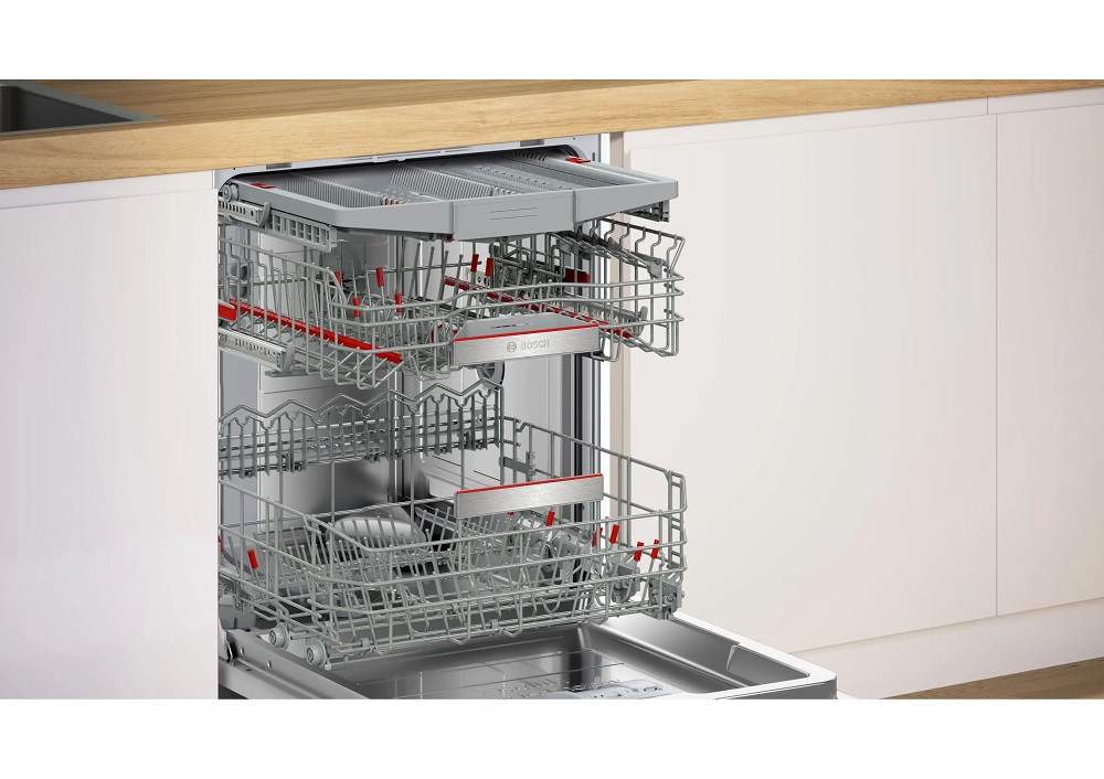 Installation view of the open Bosch dishwasher in a white kitchen unit, displaying the three-level Max Flex Pro basket system with fully extended cutlery tray, upper rack, and lower rack.
