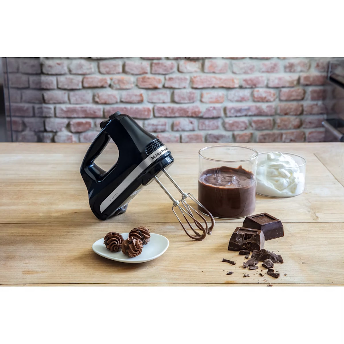 Handmixer von KitchenAid (Modell 5KHM5110EOB) in schwarzer Farbe auf einer Arbeitsfläche mit Backzutaten und -helfern