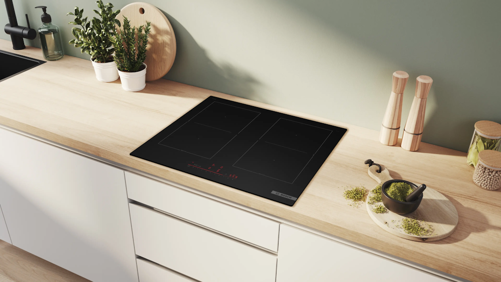 Bosch PVQ61CHB1E Induktionskochfeld eingebaut in helle Holzarbeitsplatte, umgeben von Küchenutensilien