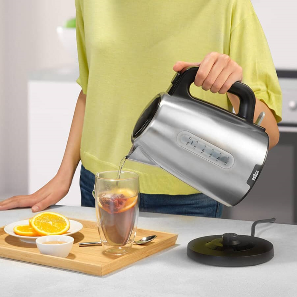 Eine Person gießt heißes Wasser aus dem Braun PurShine Wasserkocher in ein Teeglas ein; Fokus auf den ergonomischen Griff.