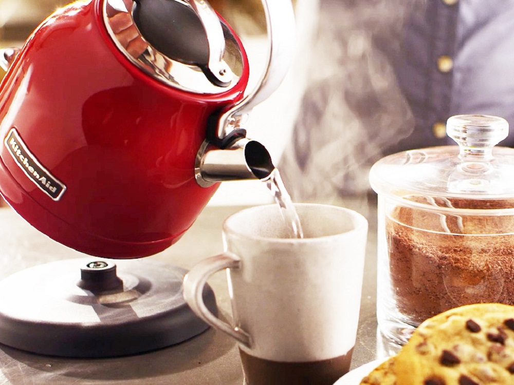 Praktisches Befüllen des Wasserkochers KitchenAid 5KEK1222EER Wasserkocher in Empire-Rot gießt Wasser in Tasse