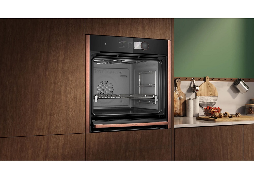 Einbau-NEFF Backofen in dunkler Holzfront mit Kupferleisten neben einer Arbeitsplatte mit frischem Basilikum und Tomaten.