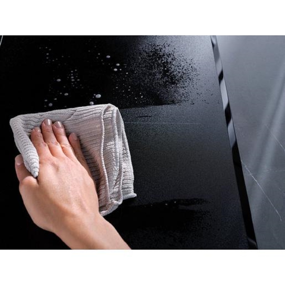 Eine Hand wischt mit einem grauen Mikrofasertuch über das matte, kratzresistente Kochfeld.