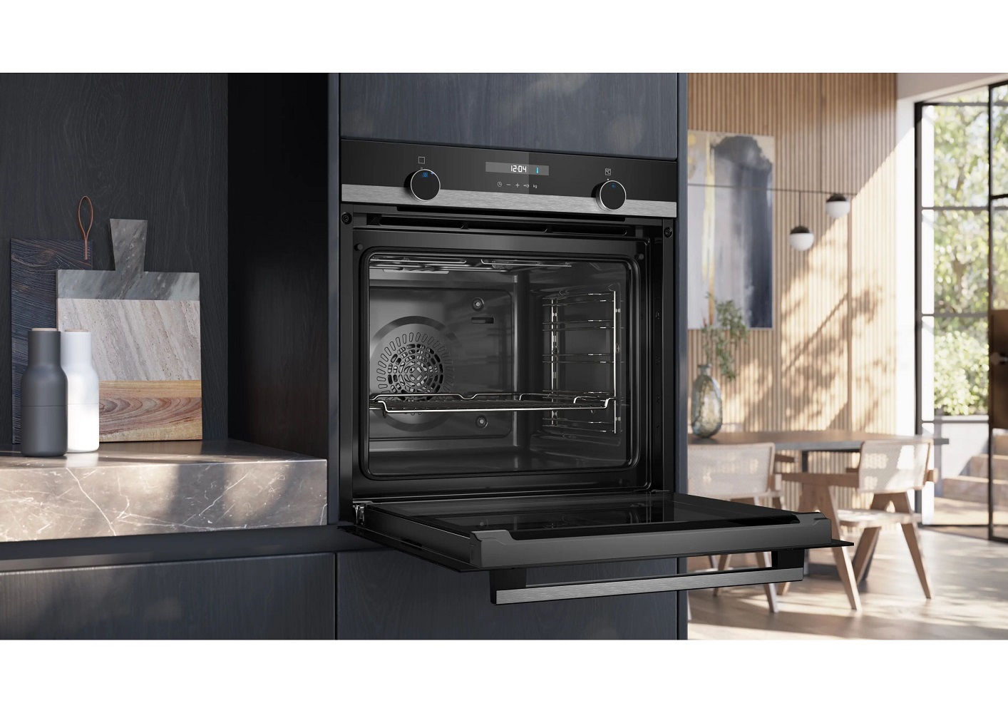 Schräge Seitenansicht eines in eine dunkle Küche eingebauten Siemens Backofens mit geöffneter Tür und Blick auf das Backblech im Inneren.