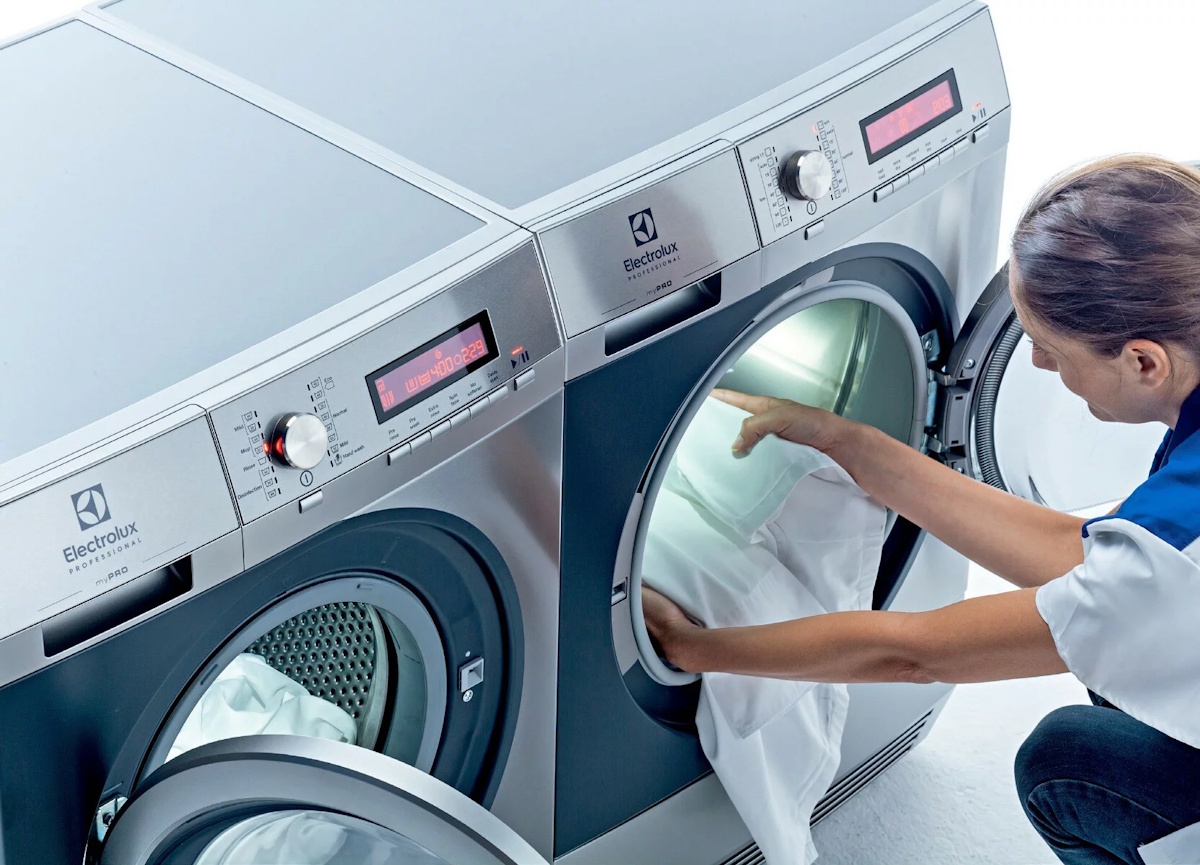 Eine Person lädt voluminöse Textilien durch die große Türöffnung in die beleuchtete Trommel des Electrolux Geräts.