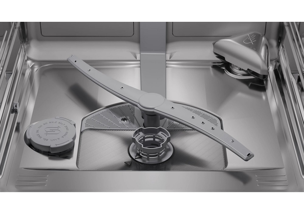 Technical interior view of the stainless steel dishwasher tub floor, showcasing the gray rotating spray arm, the fine three-piece filter system, and the salt reservoir cap on the left.
