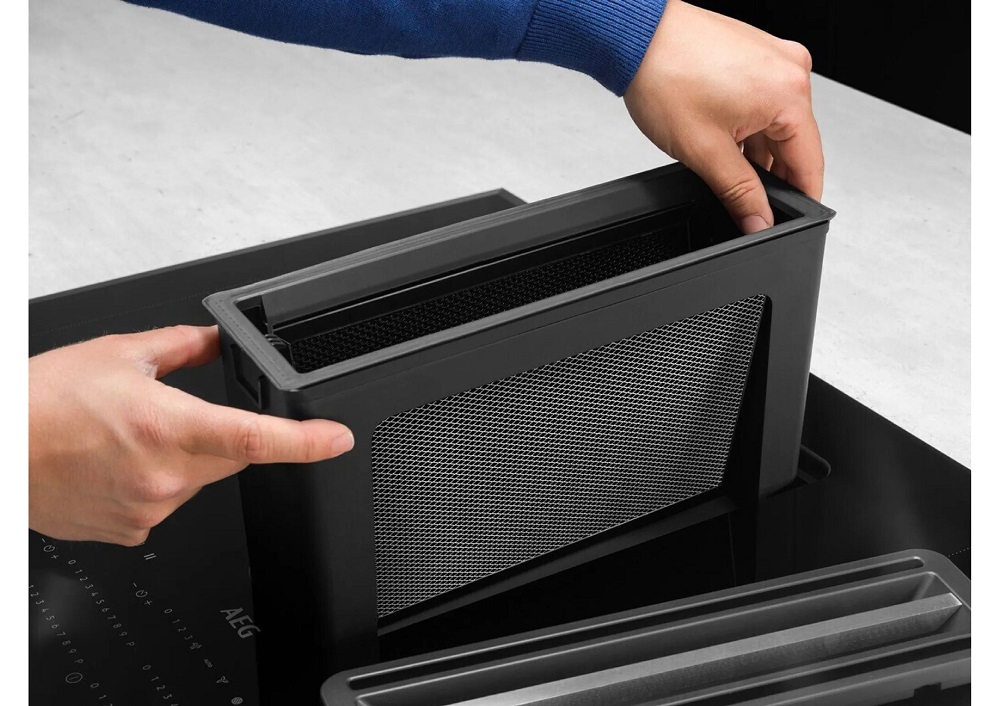 A person removing the 2-in-1 filter from the integrated extractor fan of the AEG hob for cleaning.