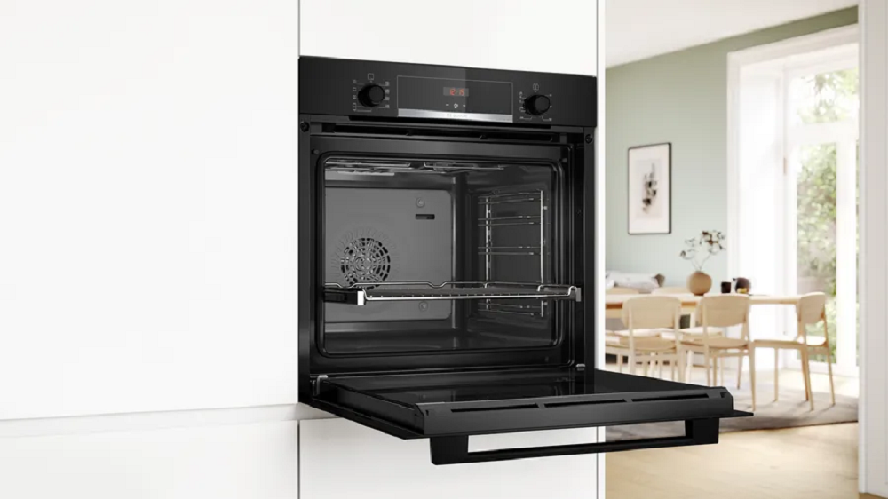 Black Bosch built-in oven with an open door in a modern white kitchen showing the interior cavity.