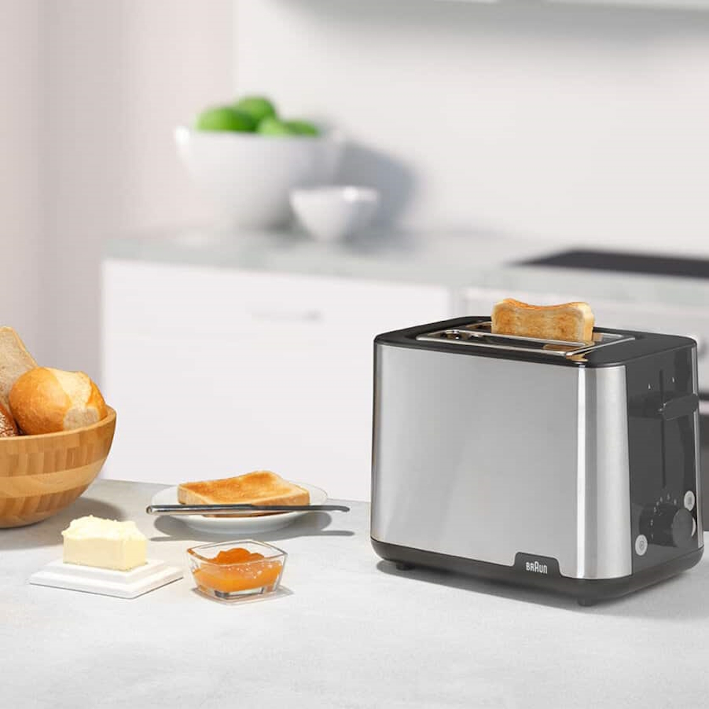 The Braun PurShine toaster on a light-colored kitchen counter next to fresh rolls, butter, and jam.