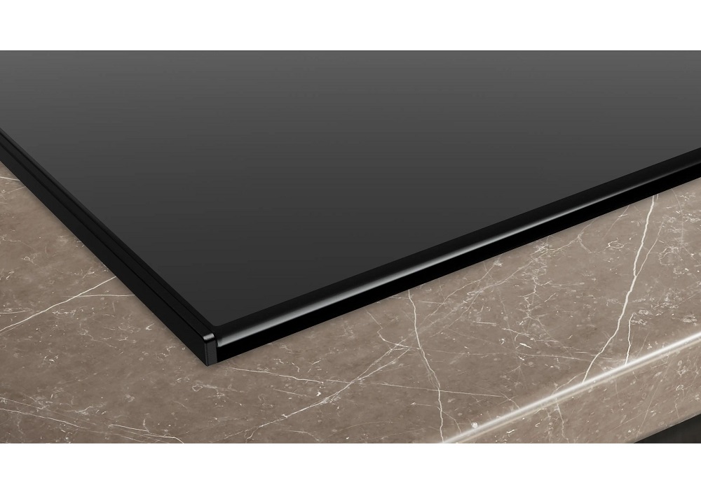 Detailed view of the precise glass edge of the hob, flush-mounted into the textured countertop.