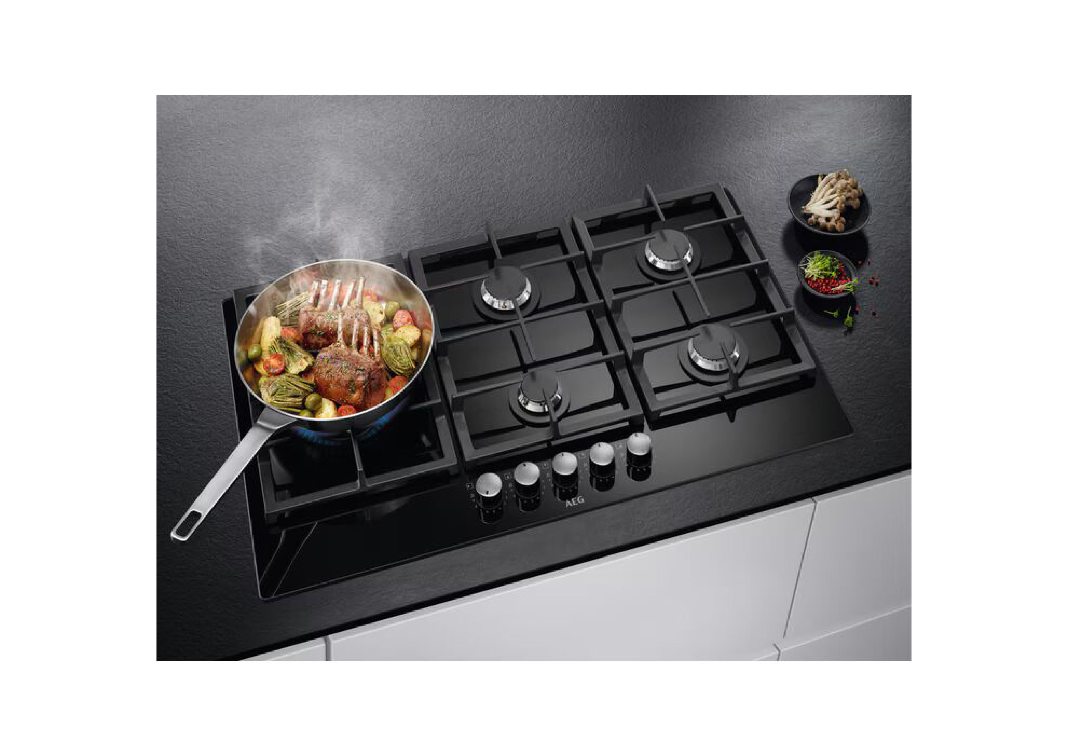 Pan with meat and vegetables on an active AEG gas hob in a kitchen setting